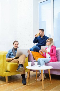 Arkadaş sohbet ve kullanarak bir smartphone, masaüstü bilgisayar, dizüstü bilgisayar koltukta otur. Sosyal medya kavramı.