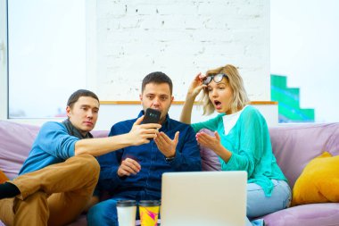Arkadaş sohbet ve kullanarak bir smartphone, masaüstü bilgisayar, dizüstü bilgisayar koltukta otur. Sosyal medya kavramı.