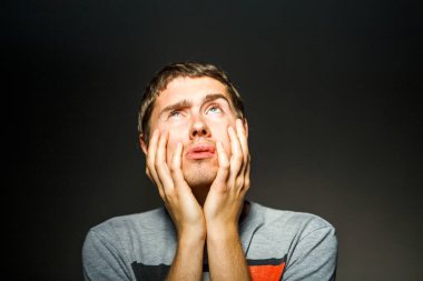 Boş siyah arka planda elleri çenesinde tişörtlü bir adamın fotoğrafı.