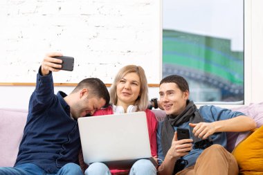 Arkadaş sohbet ve kullanarak bir smartphone, masaüstü bilgisayar, dizüstü bilgisayar koltukta otur. Sosyal medya kavramı.