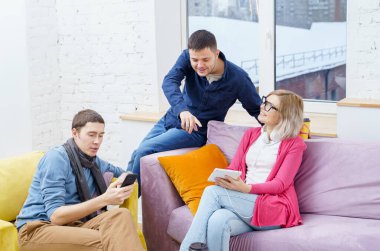 Arkadaş sohbet ve kullanarak bir smartphone, masaüstü bilgisayar, dizüstü bilgisayar koltukta otur. Sosyal medya kavramı.