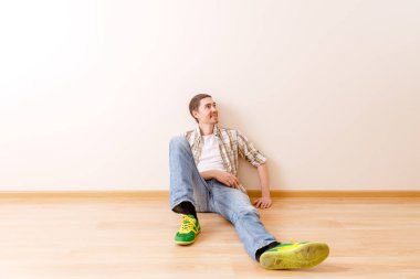 Boş bir dairede yerde oturan adamın fotoğrafı.