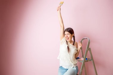 Merdiven yanında fırça ve boş pembe duvara sürtünen neşeli bir kadın resmi. Metin için yer.