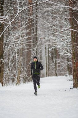 Kışın ormanda koşan genç sporcunun fotoğrafı.