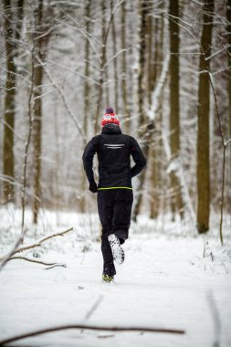Fotoğraf, kış ormanlarında ağaçların arasında koşan bir atletin fotoğrafı.