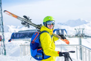 Omzunda kayak olan kask takan sportif bir adamın füniküler fonda çekilmiş fotoğrafı.