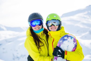 Kış aylarında dağların arka planında snowboard yapan kadın ve erkeğin fotoğrafı.