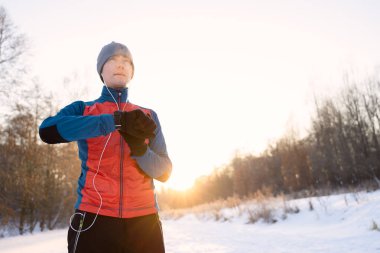 Kulaklıkla sıcak spor giysiler giyen koşucu modern akıllı saate bakıyor ve kış eğitiminde harcanan kalorileri sayıyor.