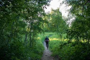 Ormanda yol boyunca kask takan bisikletli bir kadının fotoğrafı.