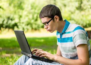 Çalışan öğrenci dizüstü bilgisayarda ağacın altında oturuyor.