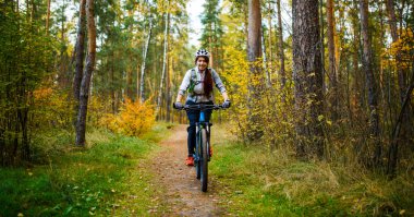 Güz ormanında bisiklet süren kasklı bir kızın fotoğrafı.