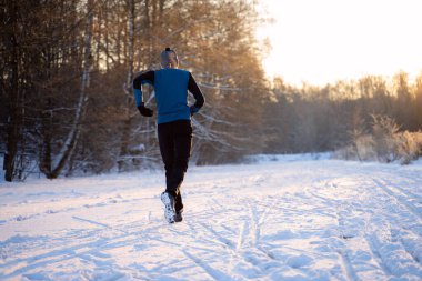 Spor giyimli bir adamın görüntüsü, kış ormanlarında koşan kırmızı şapkalı.