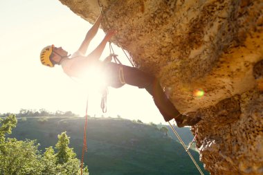 Kask takmış kayalıklara tırmanan bir adam resmi. Güneş ışığı etkisi.