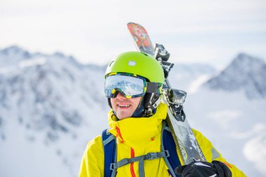 Dağın arka planında kayaklı gözlük takan bir adamın fotoğrafı.