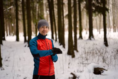 Sıcak spor giysiler giyen koşucu modern akıllı saate bakar ve kış boyunca açık havada yapılan eğitimlerde harcanan kalorileri sayar.