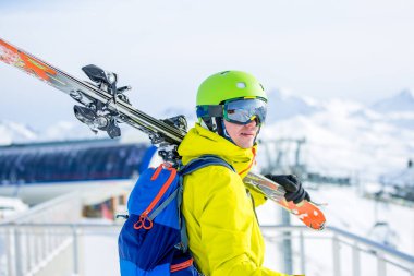 Omzunda kayak olan kask takan sportif bir adamın füniküler fonda çekilmiş fotoğrafı.