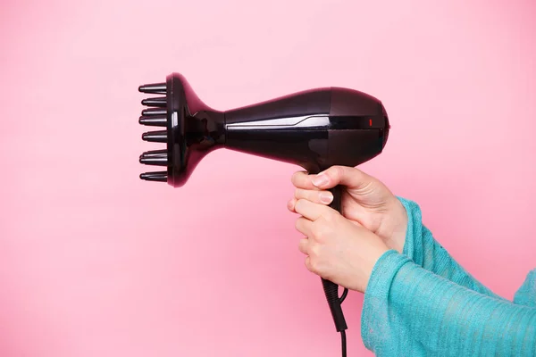 Secador de cabelo preto na mão de uma mulher em um fundo rosa