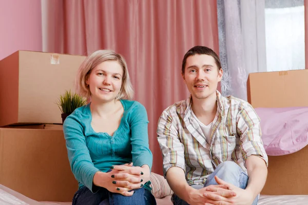 新しいアパートの段ボール箱の間にベッドに座って幸せな男性と女性のイメージ — ストック写真