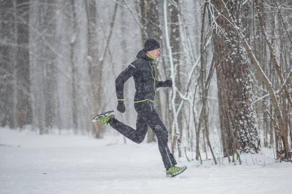 冬の森を走るスポーツウェア姿の男の横からの写真 — ストック写真