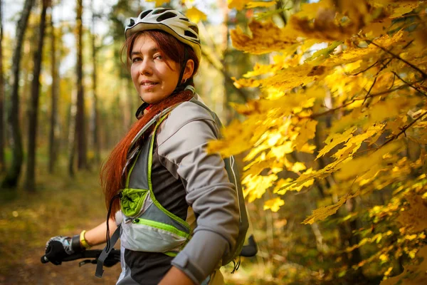 Photo of girl in helmet and sports clothes on bicycle in autumn forest