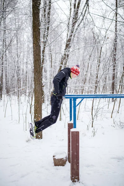 Image of sports man on horizontal bar in winter at woods by day