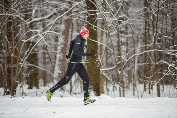 スポーツウェアの男の側からの画像 冬の森の中で実行中の赤いキャップ — ストック写真
