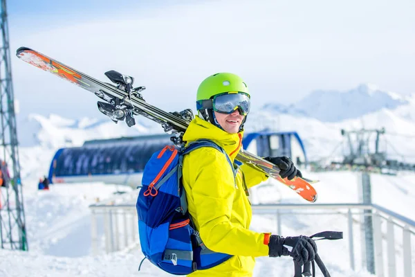 照片上的运动健将头戴安全帽 肩膀上有滑雪板 白天在滑稽的背景下 — 图库照片