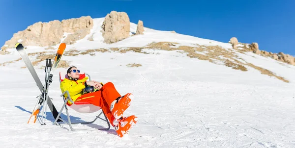 图为白天 在雪山的背景下 一个运动员坐在滑雪板旁边的椅子上 手握大棒 — 图库照片