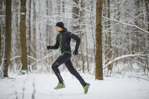 冬の森を走るスポーツウェア姿の男の横からの写真 — ストック写真