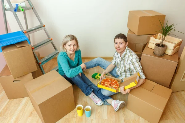 新しいアパートの段ボール箱の中でピザを食べる女性と男性の写真 — ストック写真
