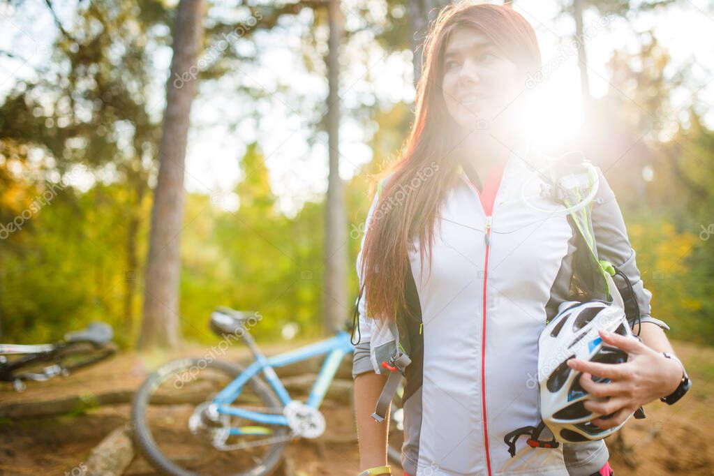 Image of young athlete with helmet on background of bicycle at autumn forest in afternoon. Sunlight effect