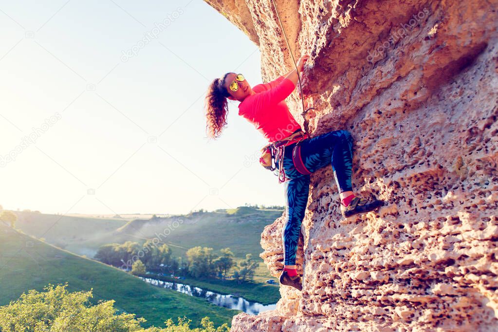 Photo of woman in sunglasses clambering over rock up at summer day