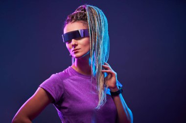 Güneş gözlüklü at kuyruklu genç kadın neon ışıklı kameraya bakıyor.