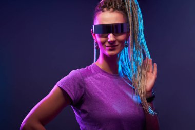 Güneş gözlüklü at kuyruklu genç kadın neon ışıklı kameraya bakıyor.