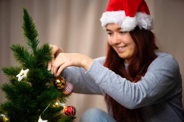 Noel Baba şapkalı mutlu kadın yeni yıl ağacını süslüyor.