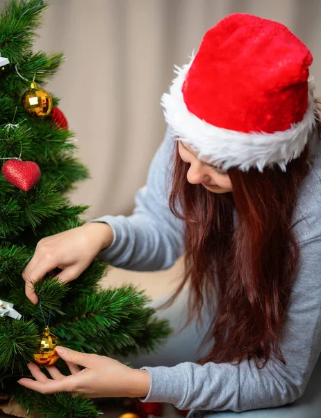 Szczęśliwa kobieta w kapeluszu Mikołaja dekoruje Nowy Rok drzewo — Zdjęcie stockowe