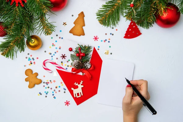 Фото красного конверта, печенья, рук с ручкой, веток елочных рождественских украшений — стоковое фото