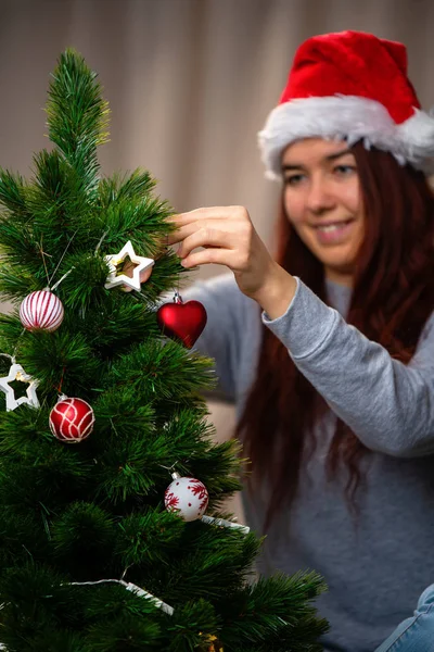サンタの帽子の幸せな女性は新年の木を飾る — ストック写真