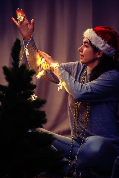 Женщина украшает новогоднюю елку горящей гирляндой — стоковое фото