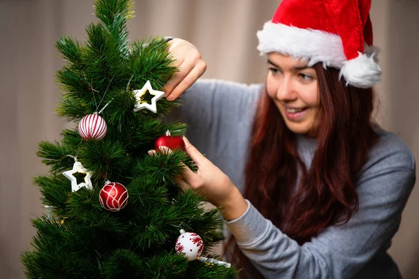 Счастливая женщина в шапке Санты украшает новогоднюю елку — стоковое фото