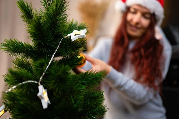 Happy woman in santa hat decorates New Year tree — Stock Photo, Image