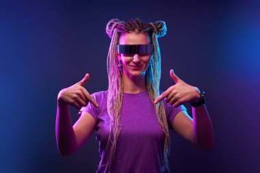 Güneş gözlüklü mutlu kız neon ışıkta kameraya bakıyor.