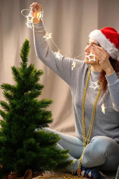 Улыбающаяся женщина украшает новогоднюю елку гирляндой — стоковое фото