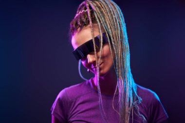 Güneş gözlüklü at kuyruklu kadın neon ışıkta kameraya bakıyor.