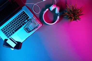 Kulaklıklı dizüstü bilgisayar, tramvay, telefon ve ödeme kartı modern neon renkli masada..