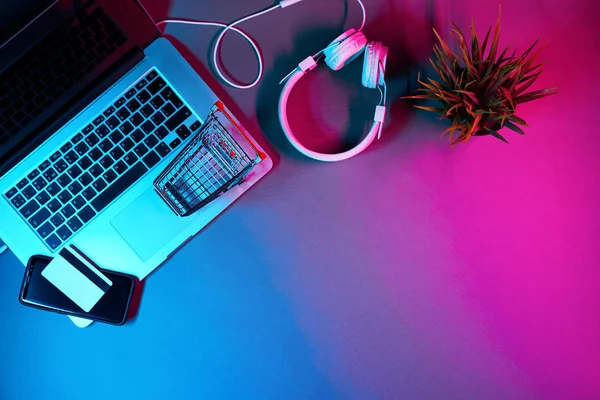 Laptop met koptelefoon, trolley, telefoon en betaalkaart op tafel in moderne neon kleuren. — Stockfoto