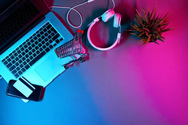 Laptop met koptelefoon, trolley, telefoon en betaalkaart op tafel in moderne neon kleuren. — Stockfoto