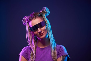 Güneş gözlüklü gülümseyen kız neon ışıkta kameraya bakıyor.