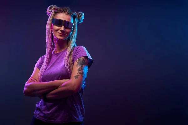 Kvinna med flätor i solglasögon tittar på kameran i neonljus — Stockfoto