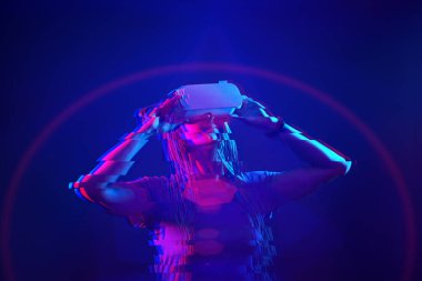 Woman is using virtual reality headset. Neon light studio portrait. Image with glitch effect.